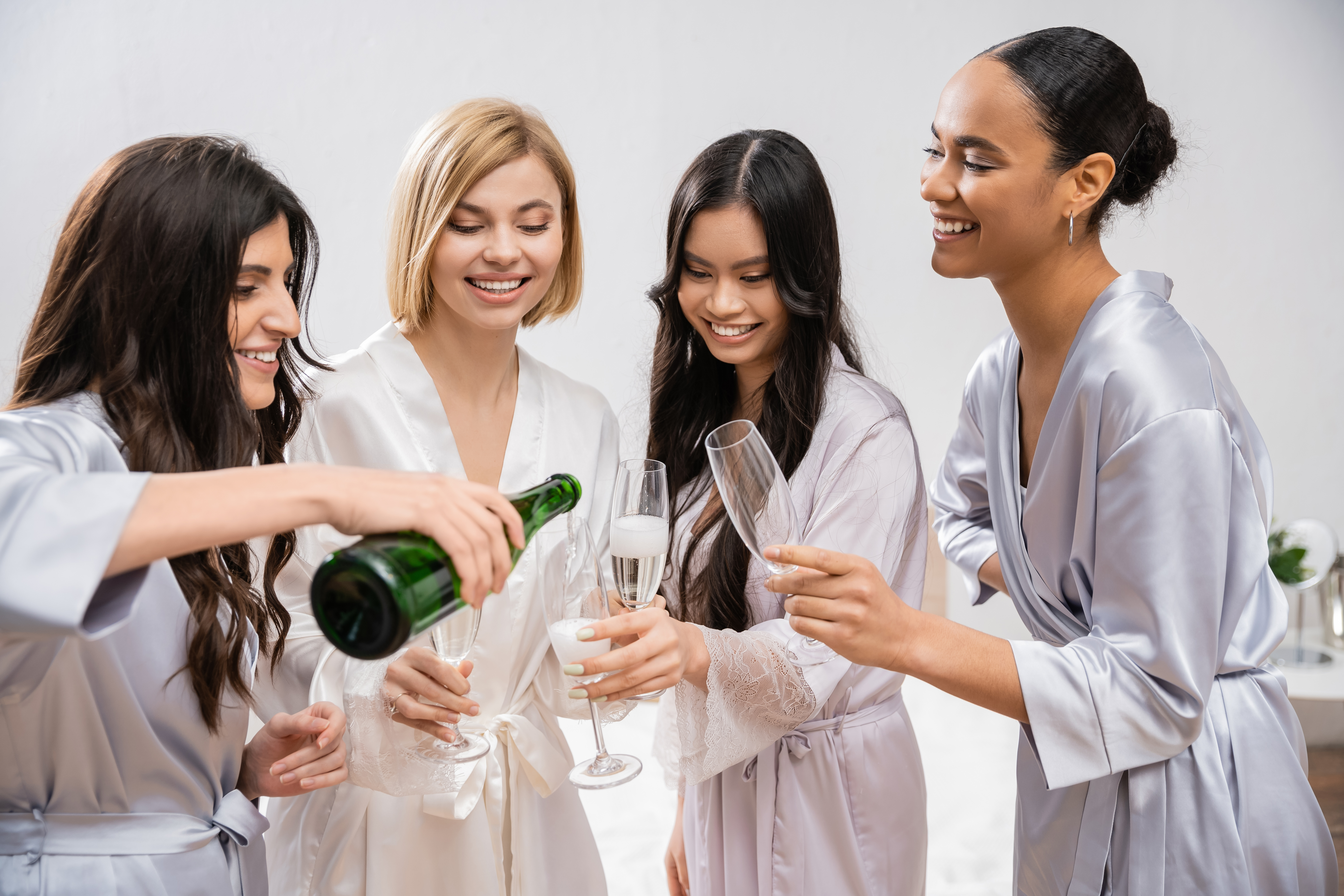 bridal shower, woman pouring champagne into glasses near interracial girlfriends, celebration