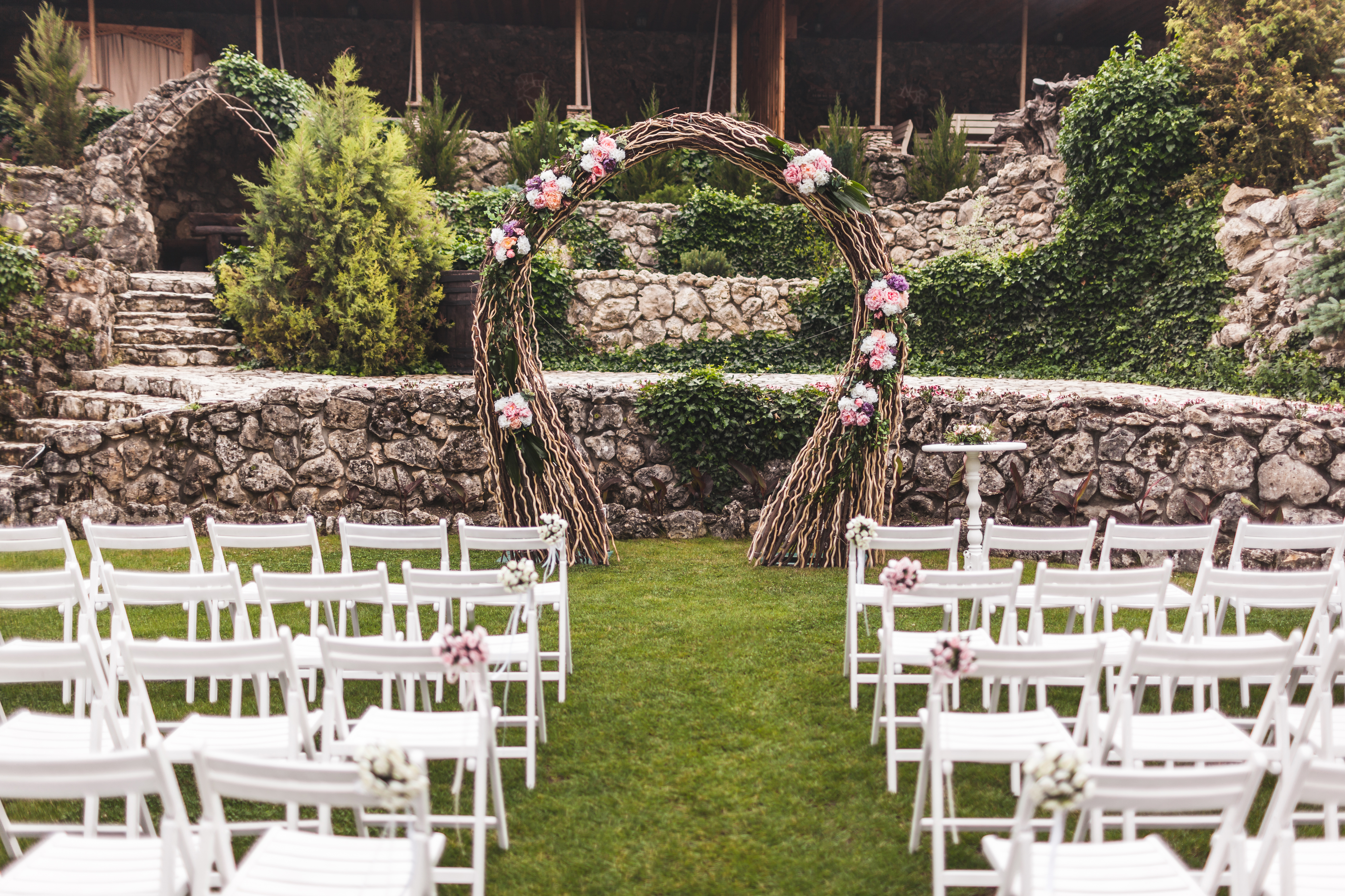 Cozy rustic wedding ceremony with flower arch and wooden white chairs in castle garden